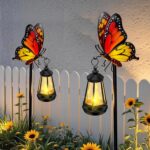 A white metal butterfly garden stake with a colorful monarch butterfly and a warm glowing solar light on its antennae, placed