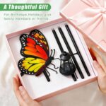A white metal butterfly garden stake with a colorful monarch butterfly and a warm glowing solar light on its antennae, placed