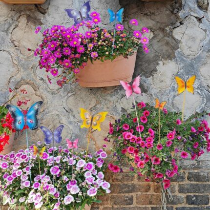 A set of 10 colorful metal butterfly garden stakes with intricate details, standing in a lush green garden bed.