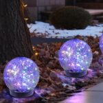 Six MLKNK solar globe lights with cracked glass texture, emitting a multicolor glow, placed in a garden setting.