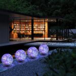 Six MLKNK solar globe lights with cracked glass texture, emitting a multicolor glow, placed in a garden setting.