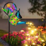 A blue butterfly solar watering can with warm white cascading fairy lights, hanging from a shepherd hook in a garden.