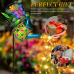 A blue butterfly solar watering can with warm white cascading fairy lights, hanging from a shepherd hook in a garden.