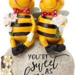 Close-up of two yellow Smadeer honey bee figurines holding flowers, sitting on a stone with an inscription.