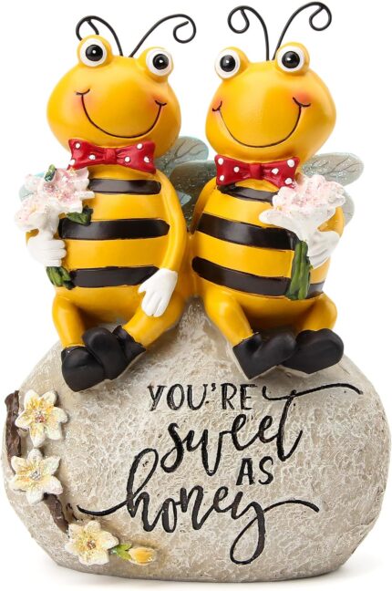 Close-up of two yellow Smadeer honey bee figurines holding flowers, sitting on a stone with an inscription.