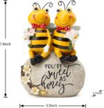 Close-up of two yellow Smadeer honey bee figurines holding flowers, sitting on a stone with an inscription.