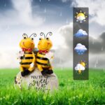 Close-up of two yellow Smadeer honey bee figurines holding flowers, sitting on a stone with an inscription.