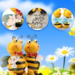 Close-up of two yellow Smadeer honey bee figurines holding flowers, sitting on a stone with an inscription.