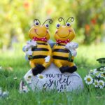 Close-up of two yellow Smadeer honey bee figurines holding flowers, sitting on a stone with an inscription.