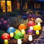 Eight colorful cracked mushroom solar lights staked in a garden bed, glowing with various LED colors.