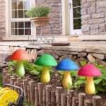 Eight colorful cracked mushroom solar lights staked in a garden bed, glowing with various LED colors.