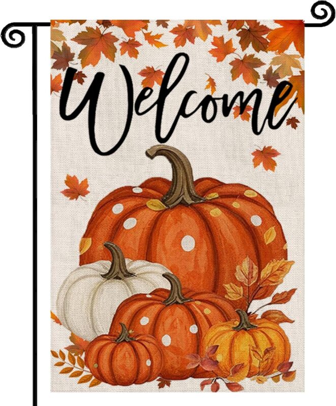 An orange double-sided garden flag featuring a large pumpkin, fallen leaves, and maple leaves, set in an outdoor garden scene