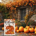 An orange double-sided garden flag featuring a large pumpkin, fallen leaves, and maple leaves, set in an outdoor garden scene